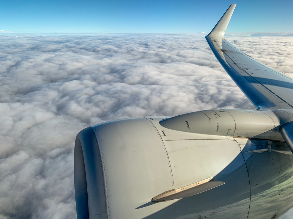 view from an airplane window of a wing, engine, clouds, and the blue horizon