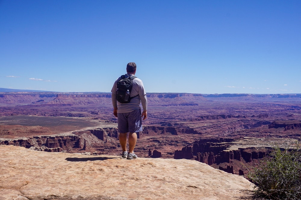 man witha  backpack standing on the ledge looking out at Canyonlands National Park in Utah